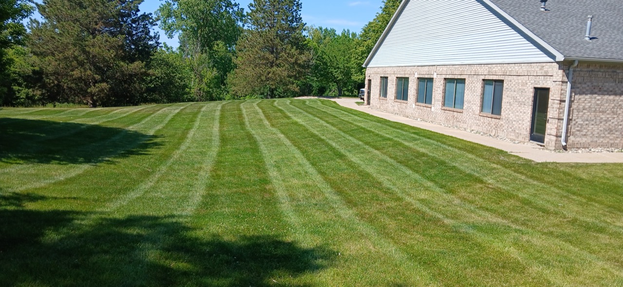 Freshly striped front lawn leading up to a brick colonial home with a curved driveway
