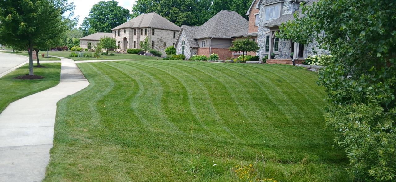 Crisp diagonal mowing stripes across a large estate lawn beside a stone-and-brick manor home